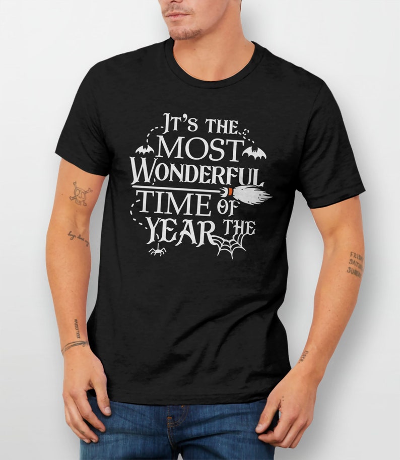 K&ouml;nnte beinhalten: Schwarzes T-Shirt mit wei&szlig;em Text, der "Es ist die sch&ouml;nste Zeit des Jahres" lautet, mit einem Besen, Flederm&auml;usen und Spinnweben.