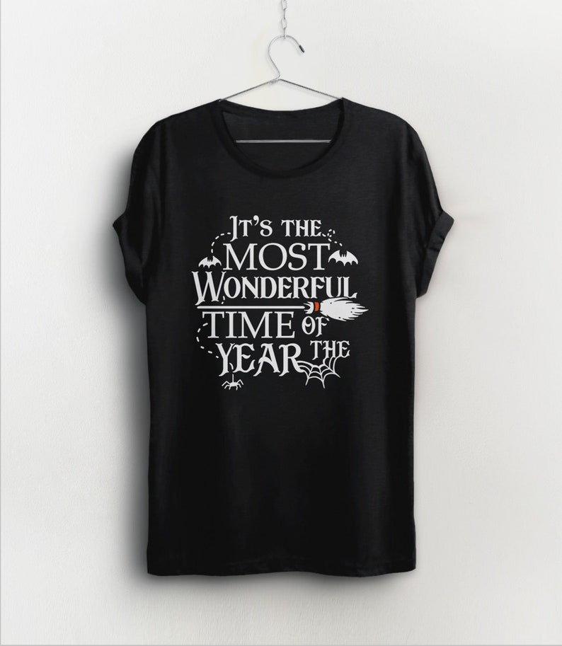 K&ouml;nnte beinhalten: Schwarzes T-Shirt mit wei&szlig;em Text, der "Es ist die sch&ouml;nste Zeit des Jahres" lautet, mit einem Besen und Flederm&auml;usen.