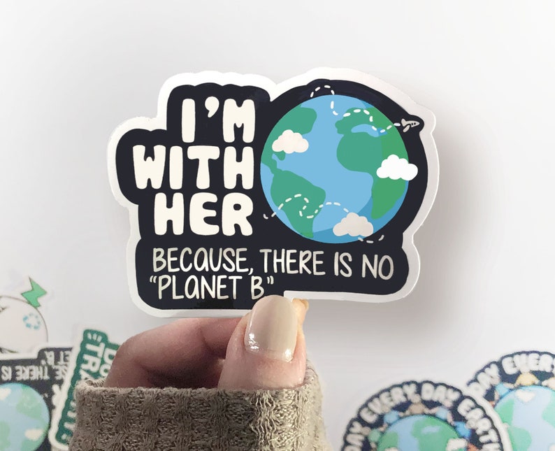 Puede incluir: Una pegatina con una ilustraci&oacute;n de dibujos animados de la Tierra con nubes y un avi&oacute;n volando sobre ella. El texto dice "Estoy con ella porque no hay "Planeta B""