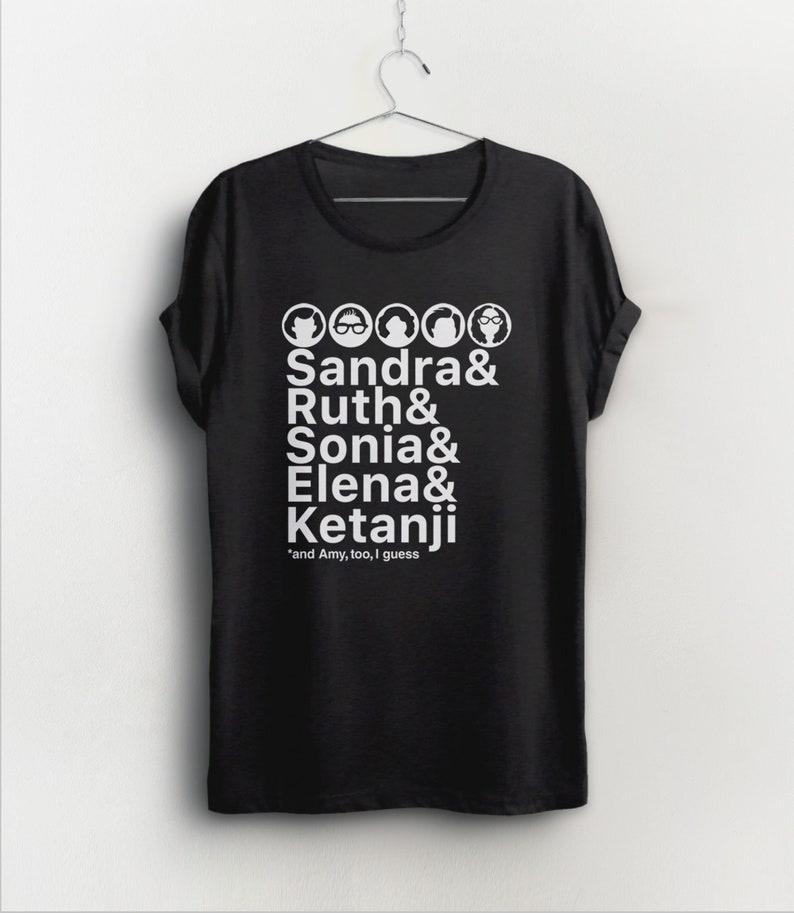 May include: Black t-shirt with white text and illustrations of female Supreme Court Justices. The text reads "Sandra & Ruth & Sonia & Elena & Ketanji" and "*and Amy, too, I guess".