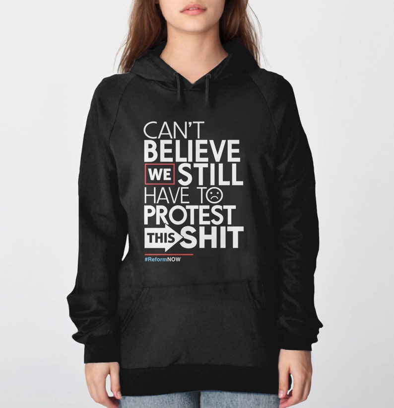 May include: Black hooded sweatshirt with white text that reads "CAN'T BELIEVE WE STILL HAVE TO PROTEST THIS SHIT." The text includes a sad face emoji and the hashtag #ReformNOW.