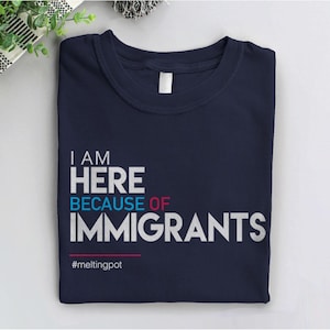 May include: A navy blue t-shirt with white text that reads "I AM HERE BECAUSE OF IMMIGRANTS" and the hashtag "#meltingpot".