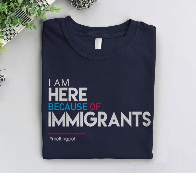 May include: A navy blue t-shirt with white text that reads "I AM HERE BECAUSE OF IMMIGRANTS" and the hashtag "#meltingpot".