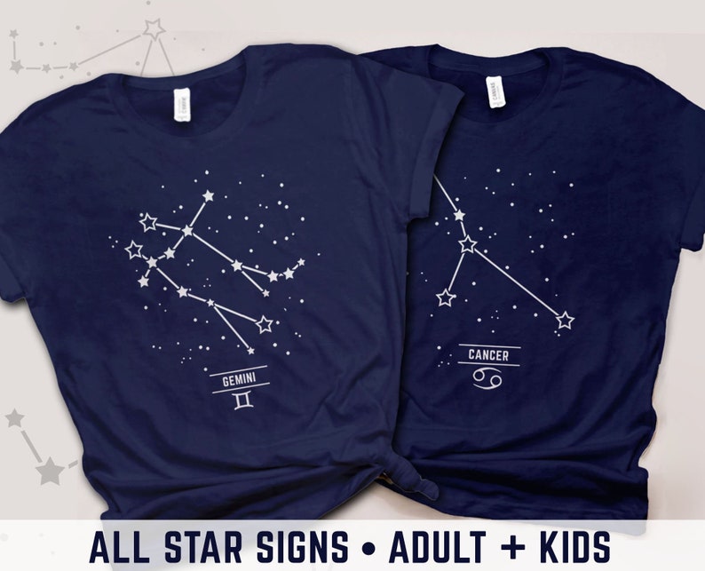 May include: Two navy blue t-shirts with white constellation designs. The left shirt features Gemini with the symbol "II" and the right shirt features Cancer with the symbol "♋". The text "ALL STAR SIGNS - ADULT + KIDS" is at the bottom of the image.