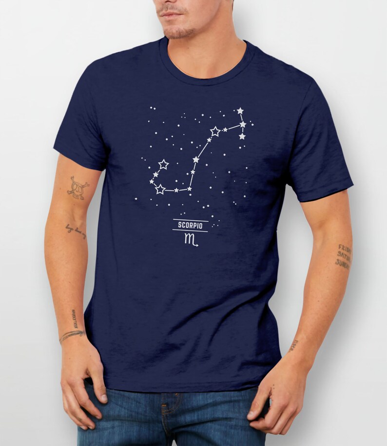 May include: A navy blue t-shirt with a white constellation design of the Scorpio zodiac sign. The text "SCORPIO" and the symbol "m" are also printed in white.
