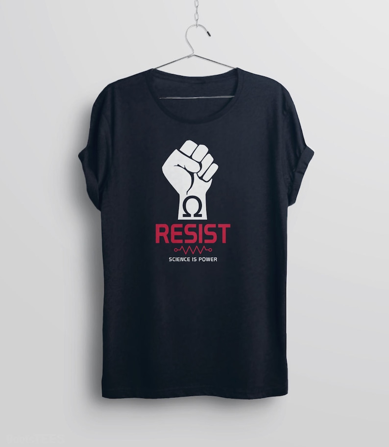 Pode incluir: Uma camiseta azul escura com um punho branco levantado no ar, um s&iacute;mbolo &ocirc;mega vermelho e a palavra "RESIST" em letras vermelhas. O texto "SCIENCE IS POWER" est&aacute; impresso em branco abaixo da palavra "RESIST".