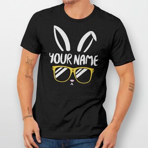 May include: Black t-shirt with a white bunny rabbit graphic wearing yellow sunglasses. The text "YOUR NAME" is printed on the shirt.