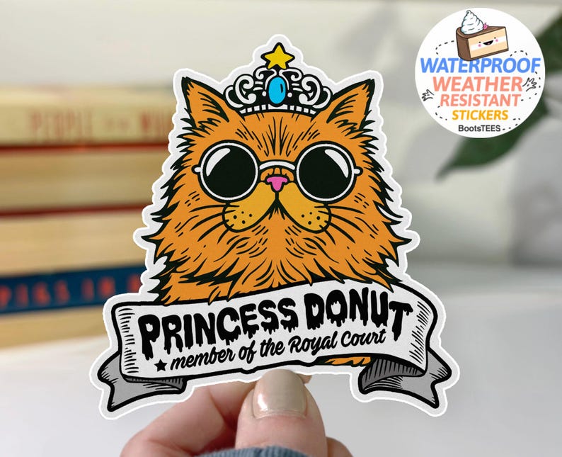 May include: A sticker featuring an orange cat wearing sunglasses and a crown. The cat has the words "PRINCESS DONUT" on a banner, with "member of the Royal Court" below. The sticker is waterproof and weather-resistant.