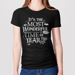 K&ouml;nnte beinhalten: Schwarzes T-Shirt mit einem wei&szlig;en Aufdruck, der "Es ist die sch&ouml;nste Zeit des Jahres" sagt, mit Flederm&auml;usen, einem Besen und einem Spinnennetz.