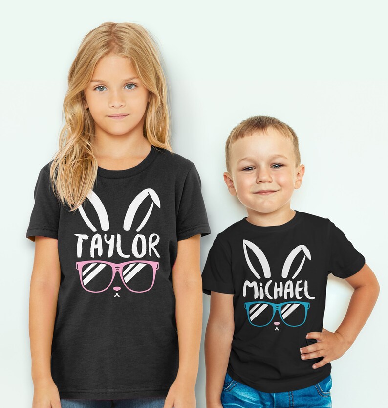 May include: Two children wearing black t-shirts with white bunny ears and sunglasses. The girl's shirt says "TAYLOR" with pink sunglasses. The boy's shirt says "MICHAEL" with blue sunglasses.