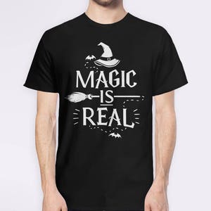 May include: Black t-shirt with a white graphic design featuring a witch's hat, a broom, and the text "Magic is Real".