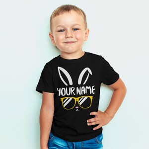 May include: A black t-shirt with a white bunny rabbit graphic wearing sunglasses. The text "YOUR NAME" is printed below the graphic.