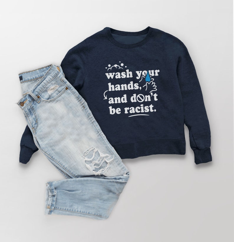 May include: A navy blue sweatshirt with the text "wash your hands, and don't be racist." in white lettering. The sweatshirt is paired with light blue jeans.