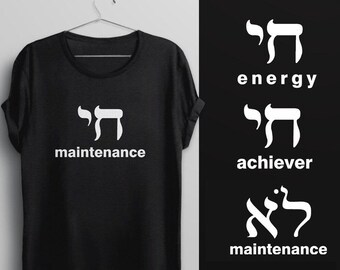 May include: A black short-sleeved t-shirt featuring the Hebrew character Chai in white, positioned above the white text maintenance. To the right, three additional white Hebrew characters are displayed with the words energy, achiever, and maintenance.