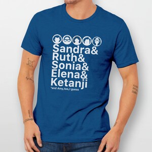 May include: A royal blue t-shirt with a white graphic of five female faces and the names Sandra, Ruth, Sonia, Elena, and Ketanji. The text *and Amy, too, I guess* is printed below the names.