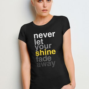 May include: Black t-shirt with the text "never let your shine fade away" in white and yellow lettering.