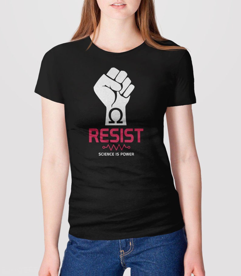 Pode incluir: Camiseta preta com um gr&aacute;fico de punho levantado branco e o texto "RESIST" em vermelho. Abaixo do texto h&aacute; um s&iacute;mbolo de resistor estilizado e o texto "SCIENCE IS POWER".