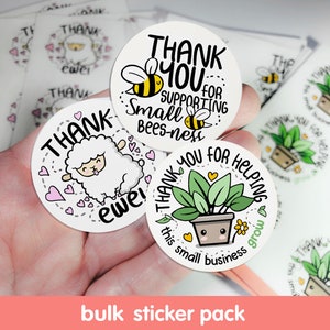 May include: A bulk sticker pack with three different designs. The first sticker features a cartoon sheep with the text "Thank ewe!" The second sticker features a cartoon bee with the text "Thank you for supporting small bees-ness." The third sticker features a cartoon plant with the text "Thank you for helping this small business grow."