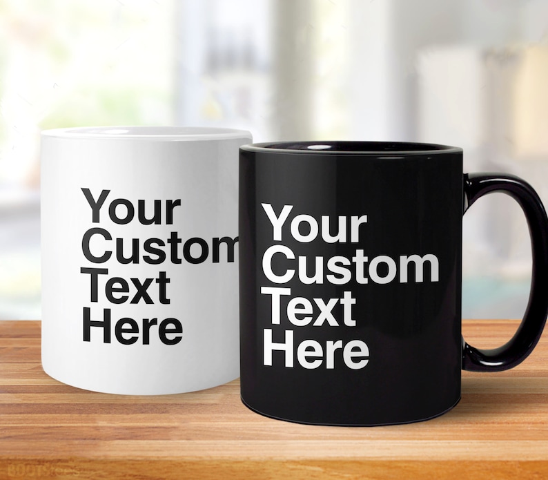 May include: Two ceramic coffee mugs, one white and one black, with the text "Your Custom Text Here" printed in black on the white mug and in white on the black mug.