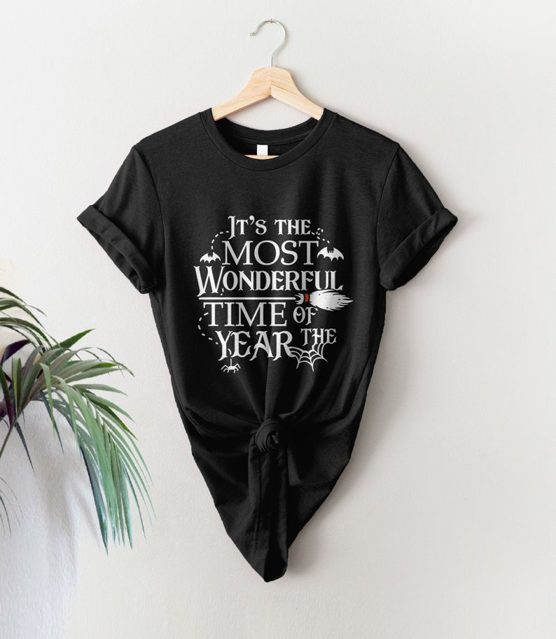 May include: Black t-shirt with white text that reads "It's the most wonderful time of the year" with a witch's broom, bats, and spiderwebs.