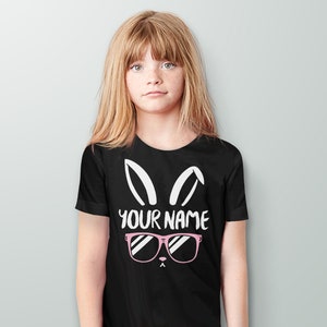 May include: Black t-shirt with a white bunny rabbit graphic wearing pink sunglasses. The text "YOUR NAME" is printed below the sunglasses.