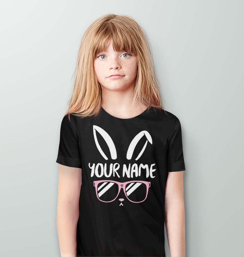 May include: Black t-shirt with a white bunny rabbit graphic wearing pink sunglasses. The text "YOUR NAME" is printed below the sunglasses.