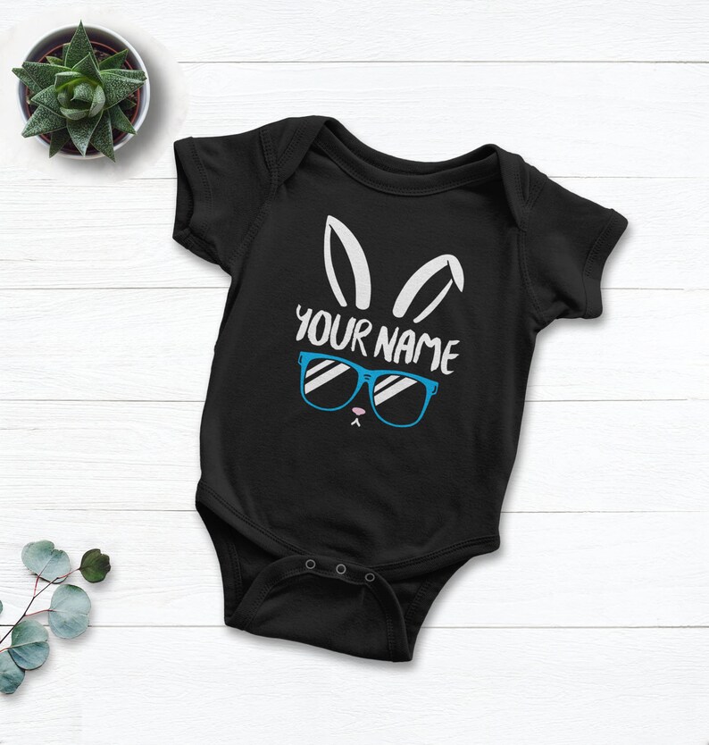 May include: Black baby onesie with a white bunny face wearing blue sunglasses and the text "YOUR NAME".