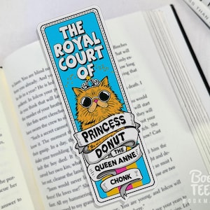 Puede incluir: Marcap&aacute;ginas rectangular con un gato de dibujos animados con gafas de sol y una corona. El marcap&aacute;ginas tiene el texto "THE ROYAL COURT OF PRINCESS DONUT THE QUEEN ANNE CHONK". El marcap&aacute;ginas est&aacute; en un libro abierto.