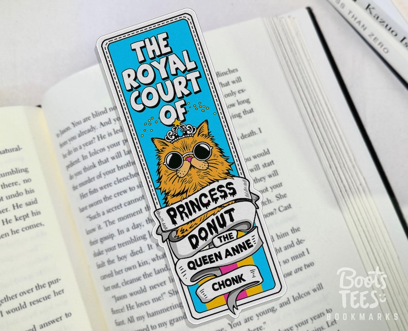 Puede incluir: Marcap&aacute;ginas rectangular con un gato de dibujos animados con gafas de sol y una corona. El marcap&aacute;ginas tiene el texto "THE ROYAL COURT OF PRINCESS DONUT THE QUEEN ANNE CHONK". El marcap&aacute;ginas est&aacute; en un libro abierto.