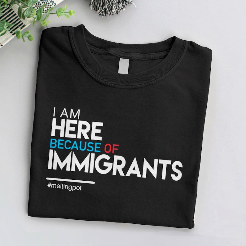 May include: Black t-shirt with white text that reads "I am here because of immigrants #meltingpot".