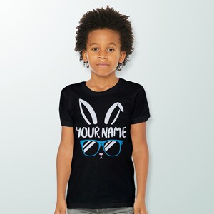 May include: Black t-shirt with a white bunny rabbit graphic wearing blue sunglasses. The text "YOUR NAME" is printed below the bunny.