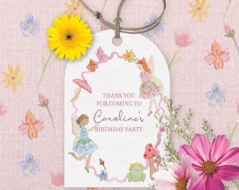 May include: A whimsical birthday party tag with the text "Thank you for coming to Caroline's Birthday Party." The tag features illustrations of fairies, mushrooms, and flowers. A yellow gerbera daisy and pink cosmos flowers are placed near the tag.