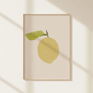 May include: A framed art print featuring a yellow lemon with a green leaf. The lemon is painted in a minimalist style against a cream-colored background. The artwork is displayed in a simple, light-colored frame.
