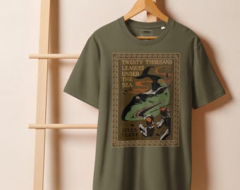 Pode incluir: Camiseta verde-oliva com uma ilustração vintage de "Vinte Mil Léguas Submarinas" de Júlio Verne. O design apresenta uma representação estilizada de um submarino e mergulhadores, emoldurada por bordas ornamentadas. O texto "Twenty Thousand Leagues Under the Sea" é visível.