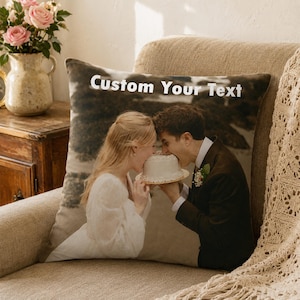 May include: A square throw pillow featuring a printed photograph of a couple in wedding attire eating a small white cake together. The text Custom Your Text is printed in white at the top of the pillow against a dark, blurred background.