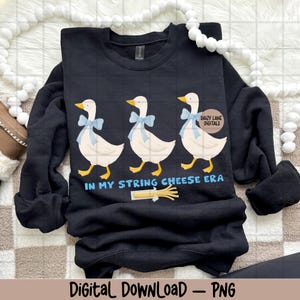 May include: Black sweatshirt with a design of three cartoon geese wearing blue bows and yellow feet, with the text "IN MY STRING CHEESE ERA." A string cheese graphic is also included. The words "Daizy Lane Digitals" are also visible.