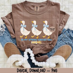 May include: A brown Comfort Colors t-shirt with a design of three geese wearing blue bows, above the text "IN MY STRING CHEESE ERA." The shirt is styled with blue jeans and brown slippers. The words "Digital DOWNLOAD - PNG" are at the bottom.