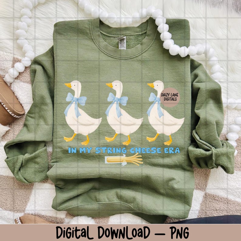 May include: An olive green sweatshirt with a design of three white geese wearing blue bows. Below the geese is the text "IN MY STRING CHEESE ERA" and a string cheese graphic. The words "Daizy Lane Digitals" are in a circle on the right.
