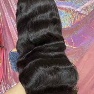 May include: A long, wavy black wig with a natural-looking hairline. The hair is styled with loose waves and has a glossy sheen. The wig appears to be made of high-quality synthetic or human hair, suitable for various occasions.