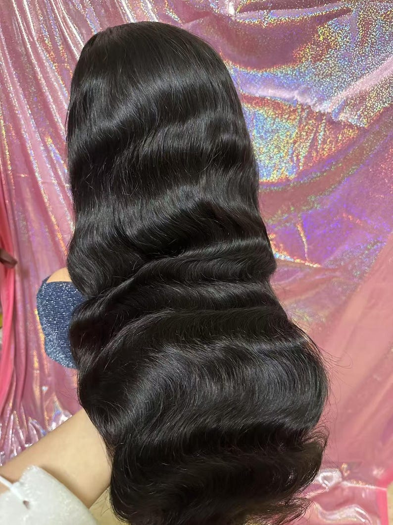 May include: A long, wavy black wig with a natural-looking hairline. The hair is styled with loose waves and has a glossy sheen. The wig appears to be made of high-quality synthetic or human hair, suitable for various occasions.