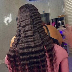 May include: Dark brown crimped hair extensions with a wavy texture. The hair is long and falls down the back. The ends of the hair have a reddish tint. The person is sitting in a pink chair.