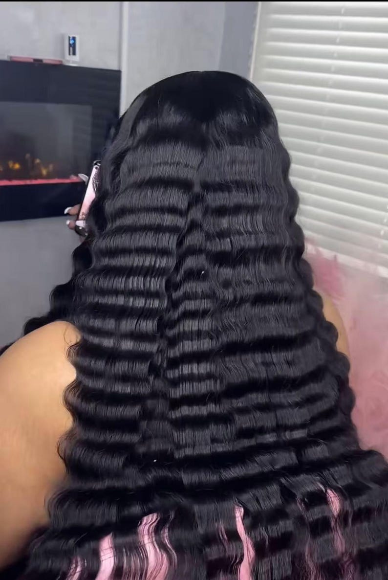 May include: A close-up of long, black wavy hair. The hair has a crimped texture, creating a series of horizontal waves. The ends of the hair have a pink hue. The image is well-lit, highlighting the texture and colour of the hair.