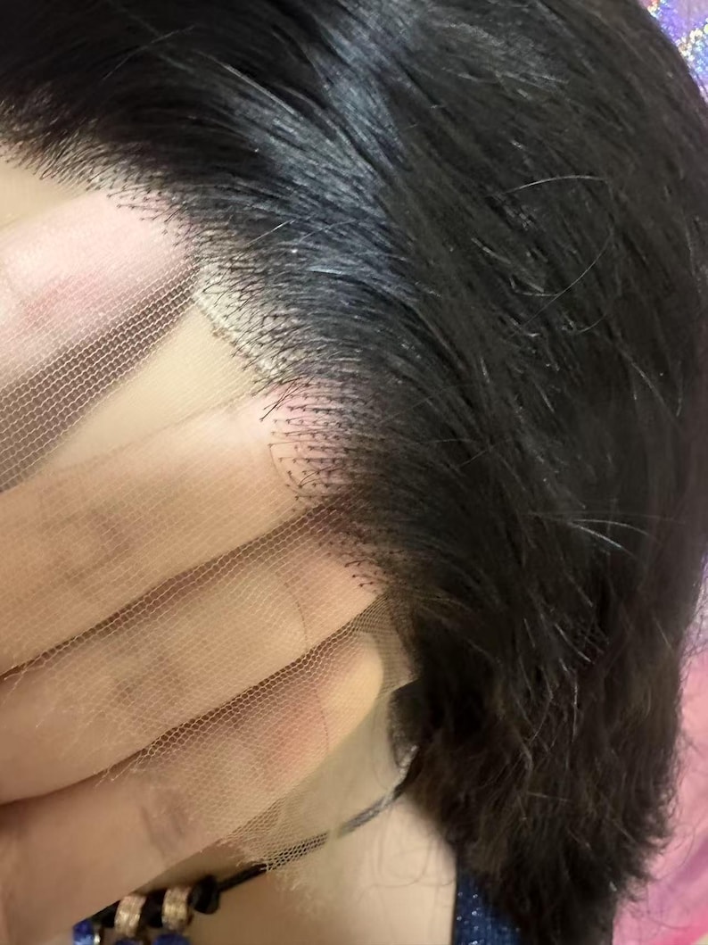 May include: Close-up of a black wig with a lace front. The wig features dark, wavy hair and a delicate, sheer lace base. The lace is a light skin tone, and the hair is neatly styled.