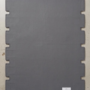 Pu&ograve; includere: Un tappeto rettangolare grigio scuro caratterizzato da un bordo dentellato a forma di pezzo di puzzle con cuciture a festone. Un'etichetta rettangolare bianca nell'angolo in basso a destra riporta il testo MAJESTIC RUGS, Hand Tufted, Cotton Canvas Backing, Made in India.