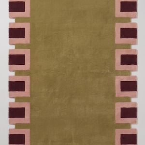 Pu&ograve; includere: Un tappeto rettangolare con un campo centrale color verde oliva tinta unita circondato da un bordo di blocchi rettangolari che si alternano tra bordeaux scuro e rosa chiaro. Il tappeto ha una consistenza morbida e include il testo Majestic Rugs.
