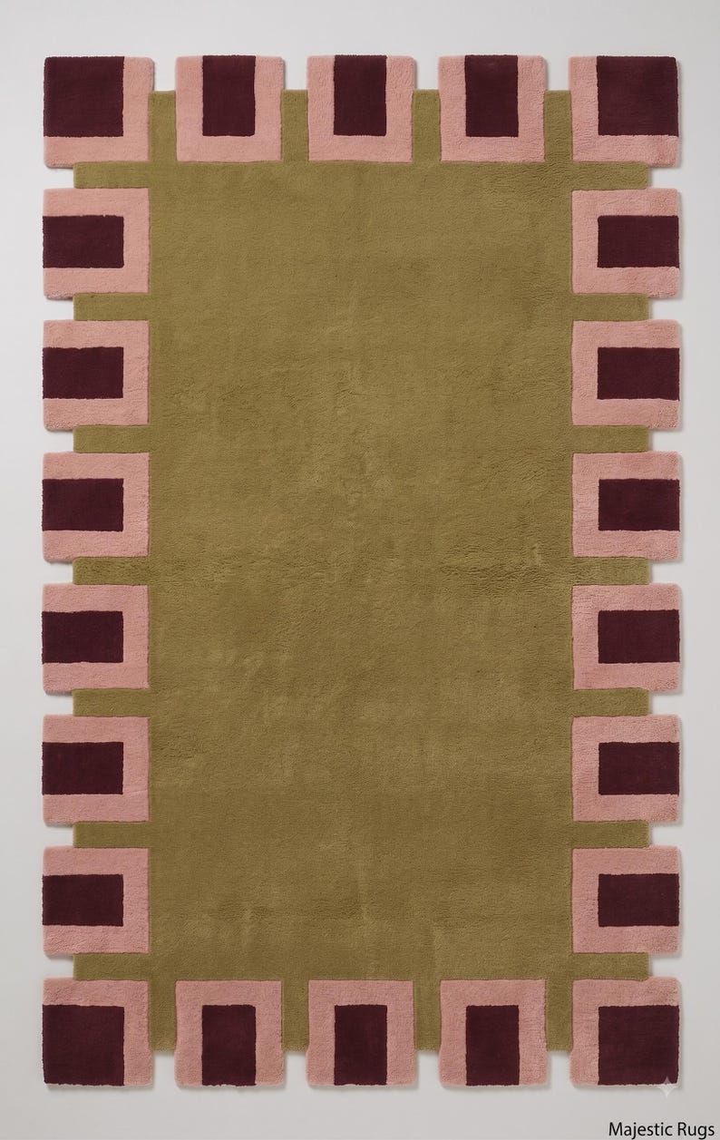Pu&ograve; includere: Un tappeto rettangolare con un campo centrale color verde oliva tinta unita circondato da un bordo di blocchi rettangolari che si alternano tra bordeaux scuro e rosa chiaro. Il tappeto ha una consistenza morbida e include il testo Majestic Rugs.