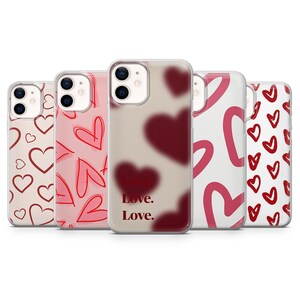 Peut inclure: Cinq coques de téléphone avec des motifs de cœurs roses et rouges. Les motifs comprennent des cœurs soulignés, des cœurs pleins et le texte "Love. Love." en rouge. Les coques sont pour smartphone.