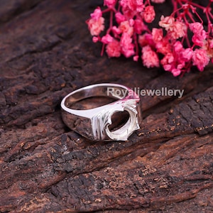 May include: A silver ring with a heart-shaped setting, perfect for a custom gemstone. The ring has a rectangular face and a polished finish. The text "Royaljewellery" is visible on the ring.