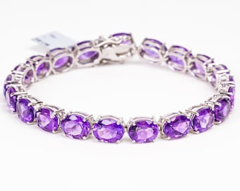 May include: A silver bracelet featuring oval-cut, vibrant purple gemstones. The gemstones are set in individual silver settings and linked together. The bracelet is displayed on a white background, showcasing its elegant design and color.