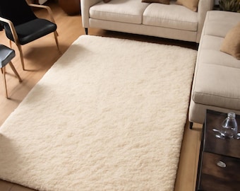 May include: A cream-colored, rectangular shag rug in a living room setting. The rug is placed on a hardwood floor, with a sofa, chairs, and a coffee table visible in the background. The rug adds a soft texture to the room.
